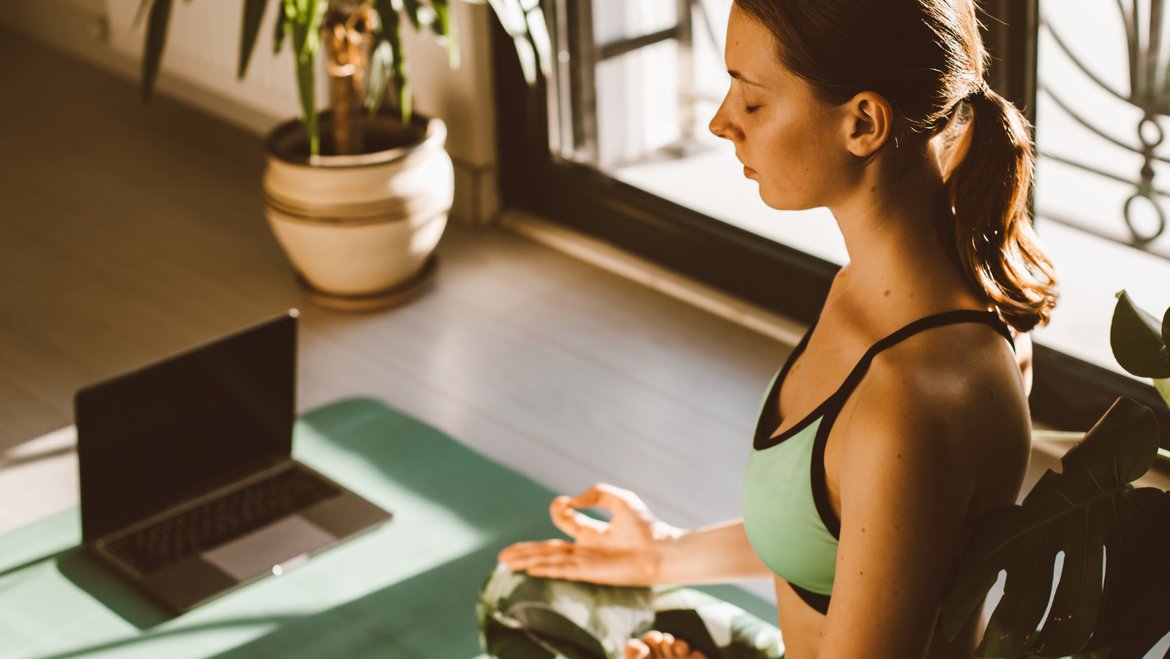 mulher sentada em posição meditativa, com um notebook em sua frente, como que sendo guiada em uma meditação